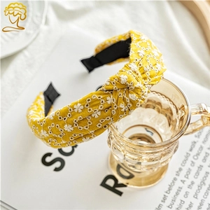 Detail of yellow fabric headband featuring white daisy embroidery and a top knot design