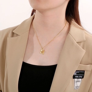 Close-up of a gold-plated H-letter pendant necklace worn with an elegant blazer