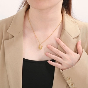 Close-up of a gold letter U pendant with rhinestones on a delicate bead chain necklace