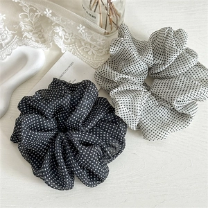 Black and white polka dot mesh scrunchies on a wooden table with lace and glass decor