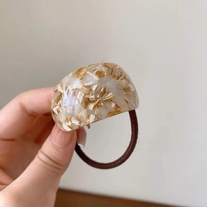 Detail of curved acetate hair tie featuring amber marble texture and brown elastic band