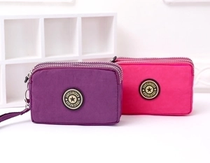 Detailed view of two nylon triple-zipper purses in purple and rose red with hand straps