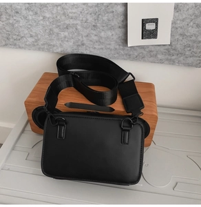Detail of minimalist black crossbody bag with wide nylon strap and matte finish texture