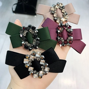 Close-up detail of elegant satin bow hair clips featuring sparkling crystal rhinestone clusters in various colors.
