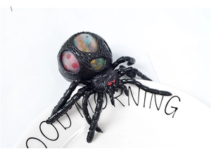 Close-up of black spider squeeze toy with colorful polka dot gel ball popping through mesh