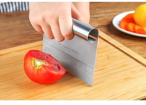 Close-up of stainless steel bench scraper with scales slicing tomatoes on wooden board