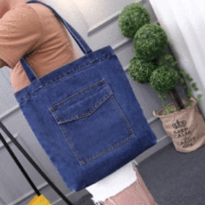 Detail of blue denim tote bag with large front pocket shown in a casual lifestyle setting