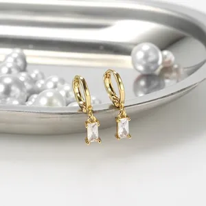 Elegant gold rectangular zircon drop earrings displayed on a polished silver tray