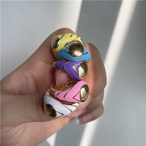 Stack of five colorful enamel eye rings in gold-plated finish on a hand under sunlight