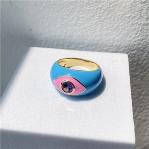 Macro shot of evil eye ring with blue enamel and pink iris detail on white stand