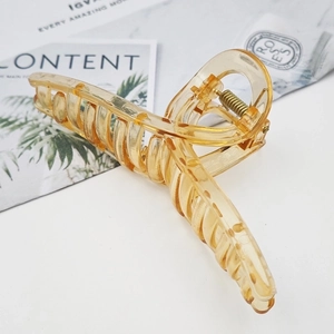 Detail view of large amber hair claw clip with golden spring on marble background