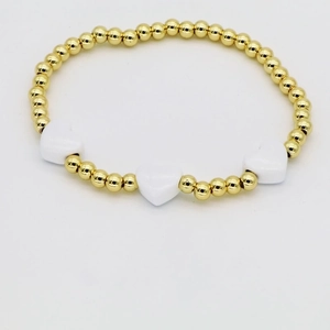 Detailed close-up of golden beaded bracelet featuring three white enamel heart charms