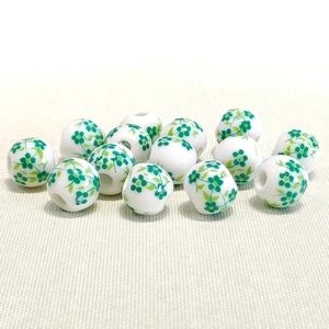 Detail of 10mm white ceramic beads with green floral pattern on textured fabric