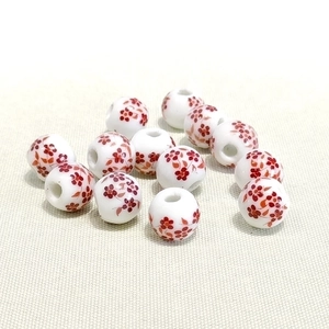 Close-up of 10mm ceramic beads with red floral patterns on white porcelain surface