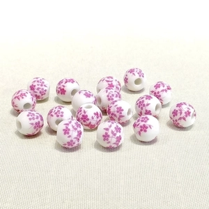 Detailed view of 10mm white ceramic beads with purple floral patterns on fabric