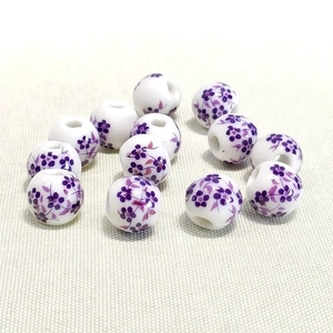 Macro shot of 10mm white ceramic beads with purple floral patterns and threading holes