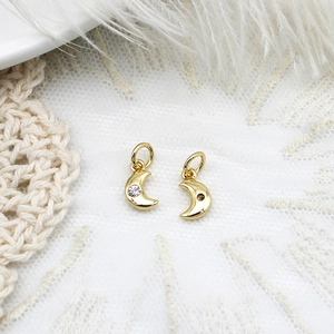 Macro shot of gold moon pendants with zircon inlay on white lace and feather backdrop