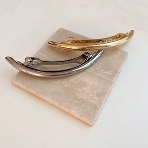 Minimalist curved metal hair clips in gold and silver finish on marble background