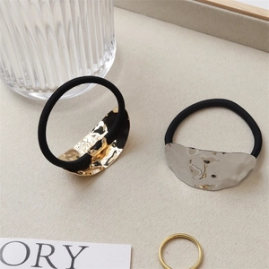 Textured gold and silver metal charms on black elastic hair ties in a minimalist tray