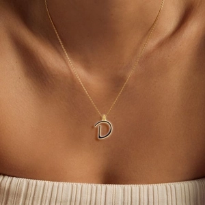 Golden necklace with black enamel letter D pendant worn by a model in soft light