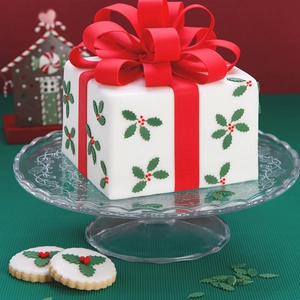 Torta a scatola regalo di Natale con fiocco rosso e foglie di agrifoglio su vetro
