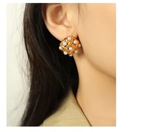 Close-up of woven gold mesh earrings with white pearl inlays on a female model