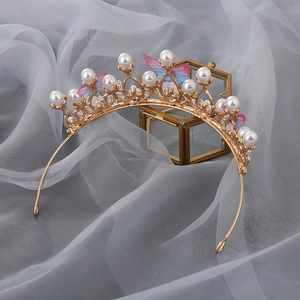 Detail of golden princess crown featuring white pearls and delicate pink blue butterflies