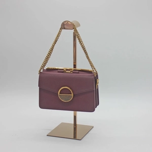 Elegant purple leather handbag with gold circular clasp and chain on metal display stand