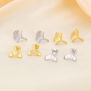 Detail of stainless steel ginkgo leaf and whale tail earrings on champagne silk fabric