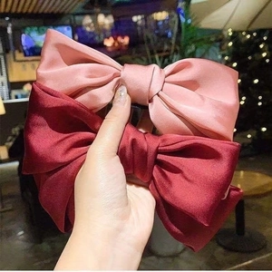 Close-up of oversized satin bow hair clips in pink and burgundy with a glossy finish