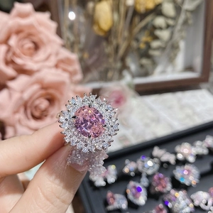 Close-up of pink oval gemstone ring with diamond halo setting on hand in jewelry box