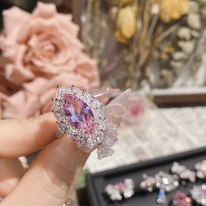 Close-up of pink marquise-cut crystal ring on finger with elegant floral background