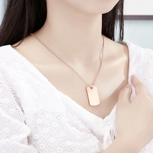 Close-up of a rose gold dog tag pendant on a beaded chain necklace worn by a model