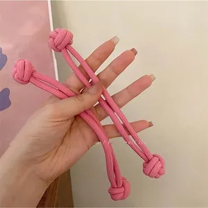 Detail showing two pink elastic hair ties with woven ball knots held by hand