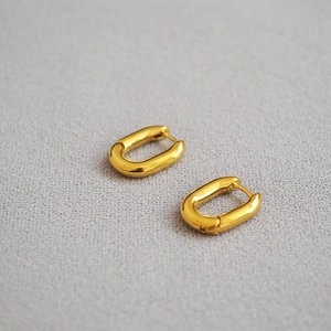 Détail de boucles d'oreilles créoles dorées en forme de U sur fond gris clair texturé