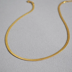 Elegant gold-plated brass flat snake bone chain necklace on a textured grey background