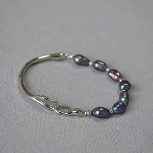 Detail view of irregular silver wave metal buckle and dark iridescent baroque pearls