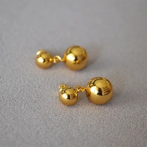 Dettaglio degli orecchini a doppia sfera d'oro lucido su sfondo di tessuto grigio