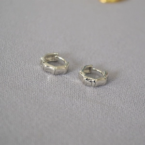 Dettaglio ravvicinato di orecchini a cerchio in argento a forma di bambù su tessuto grigio