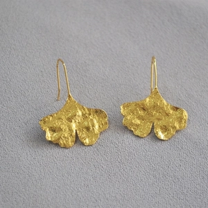 Ginkgo leaf drop earrings in gold finish with a textured surface on grey background