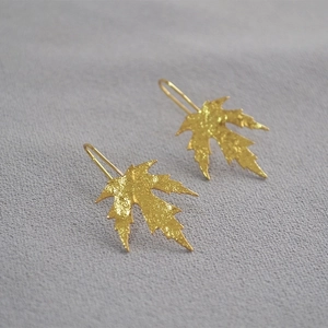 Detailed macro view of gold-plated maple leaf earrings with textured hammered finish