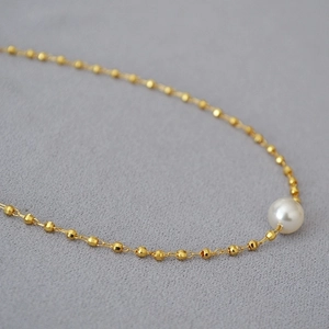 Elegant gold beaded necklace with a white pearl pendant on a soft grey background
