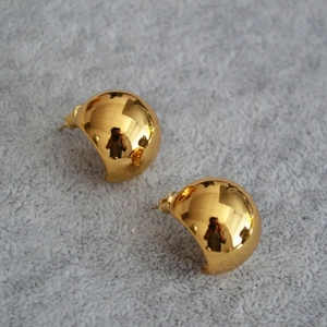 Close-up of golden hemispherical stud earrings with a high-polish mirror finish surface