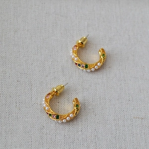 Gold-plated C-shaped twist earrings with colorful zircons and white pearls on linen