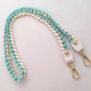 Detail of turquoise and beige woven crossbody strap with white leather and gold metal clips