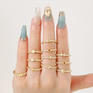 Close-up of gold plated letter rings with zircon stones worn on fingers with blue nails