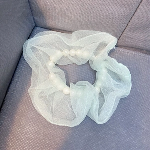 Makro-Detail von mintgrünem Organza-Haargummi mit weißen Perlen auf grauem Stoff