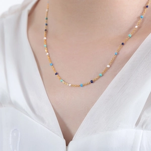 Golden titanium steel necklace with blue and white enamel beads worn on a model's neck