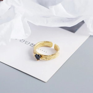 Macro detail of gold hammered ring with black heart zircon on minimalist card