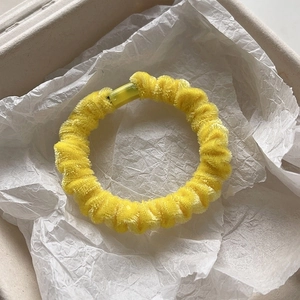 Detail view of bright yellow velvet scrunchie showing soft chenille fabric texture and closure